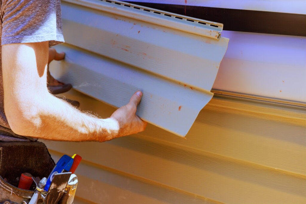 worker installs vinyl plastic siding panels on house facade