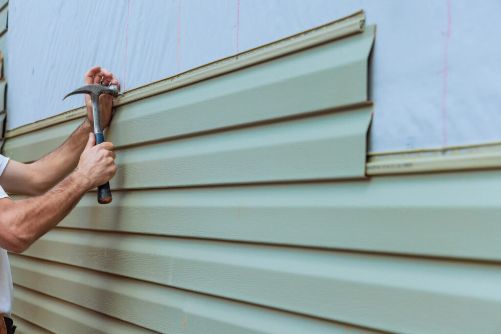 Contractor installing vinyl siding plastic panels on facade wall 